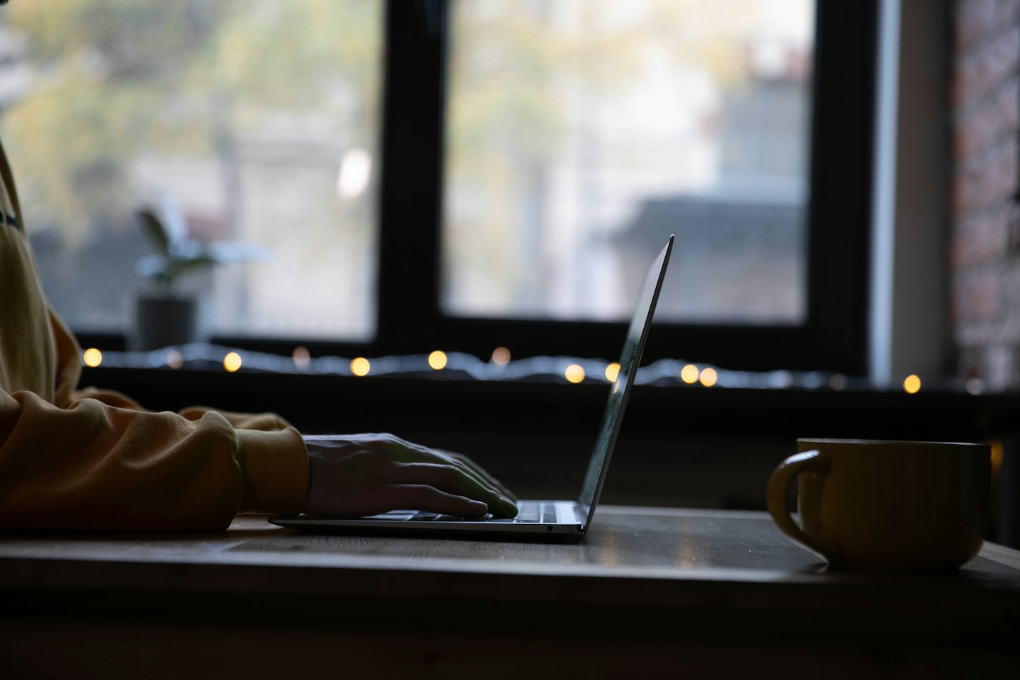 Hände tippen auf einem Laptop neben einer gelben Tasse.
