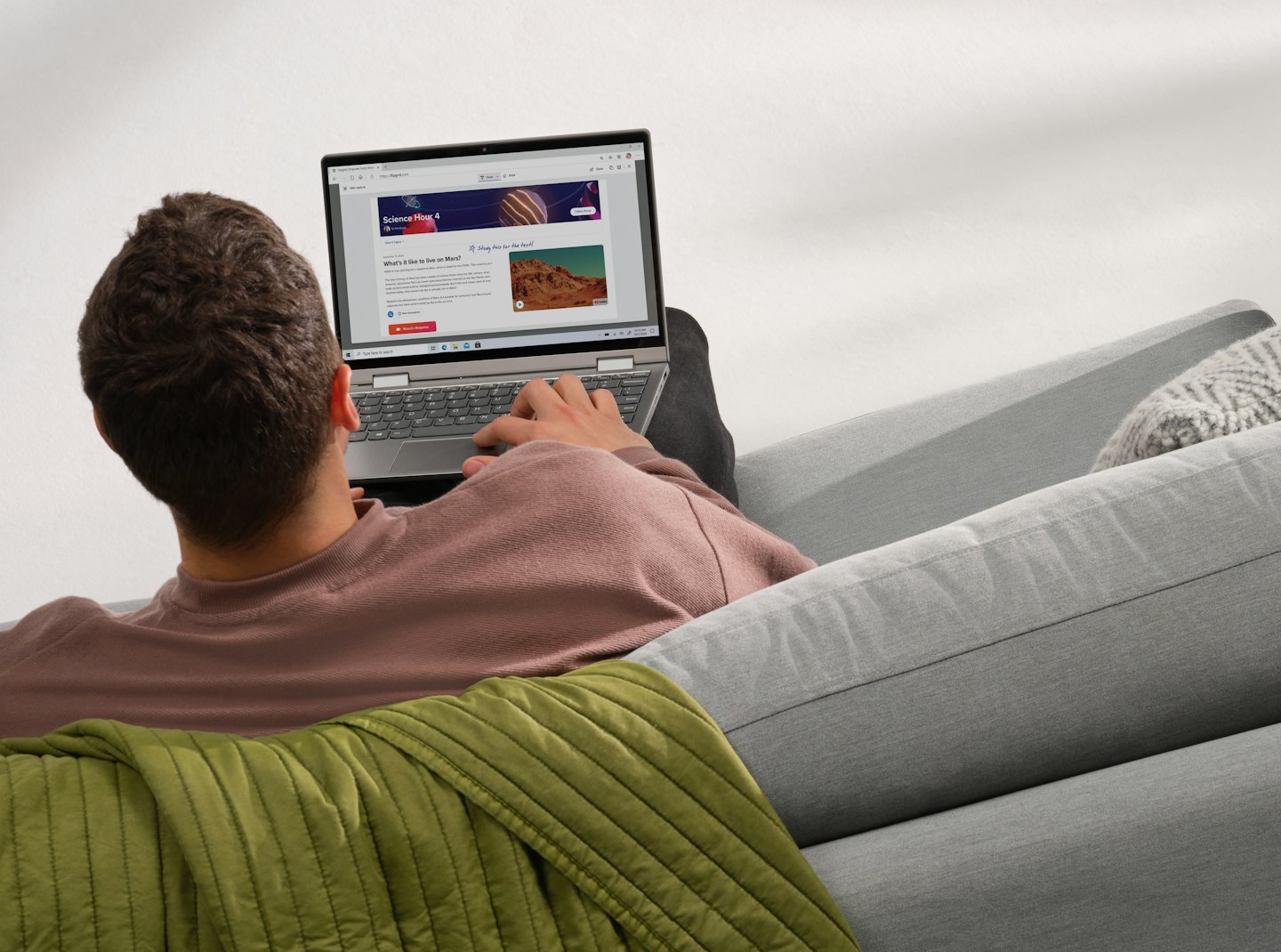 Eine Person lernt auf einem grauen Sofa mit einem Laptop.